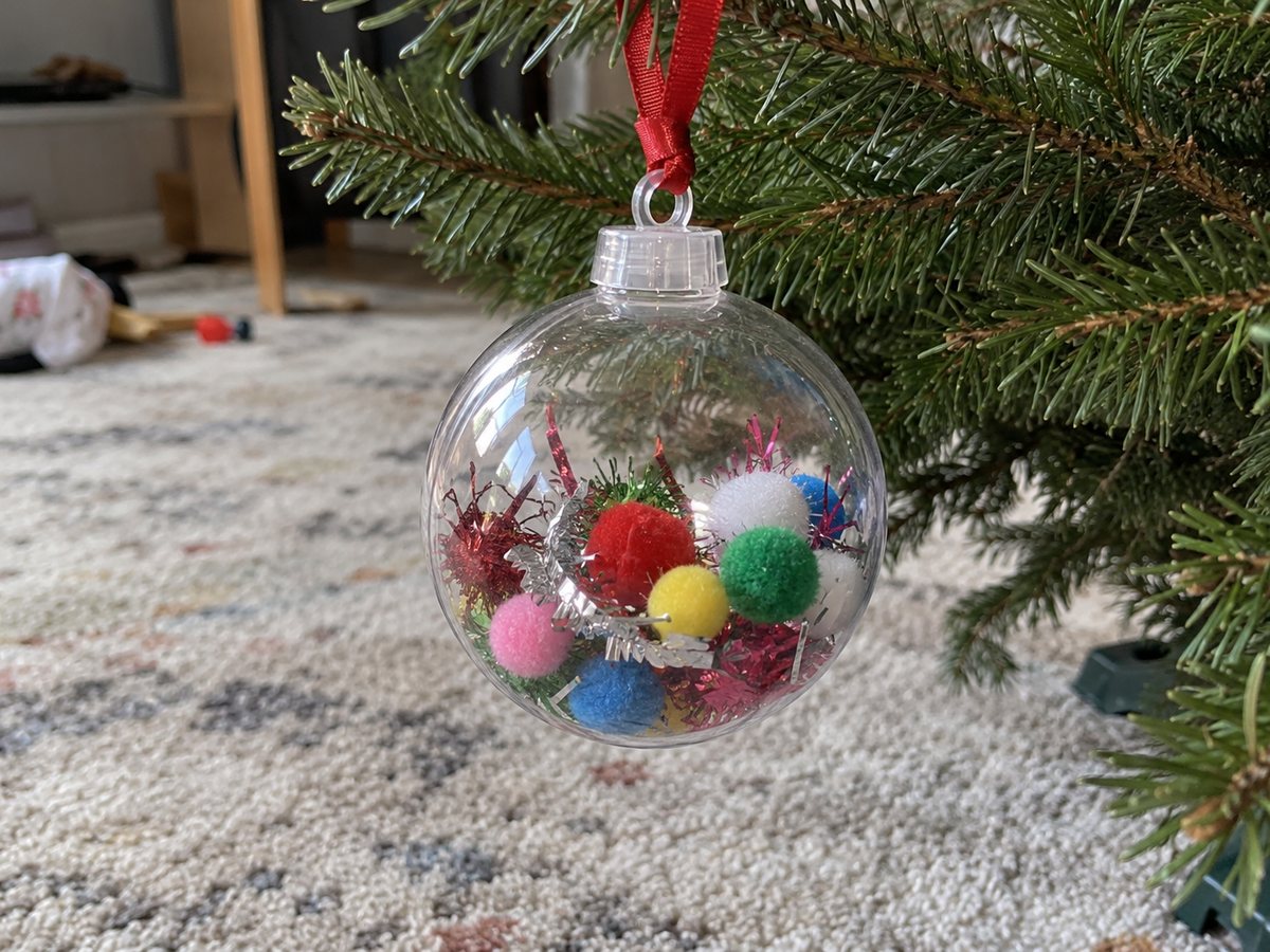 Прозрачный пластиковый шар, наполненный разноцветными помпонами и обрезками мишуры, на ленте